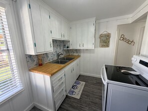 A compact kitchen with white cabinets, a wooden countertop, a built-in sink, and a white stove. - Mermaid on Murray - Rockport (Rockport)