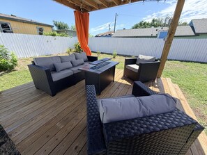 Een terras buiten met rieten meubels, waaronder een bank en stoelen, en een bijzettafeltje.