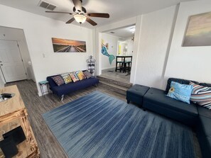 Ein Wohnzimmer mit einer Couch, einem Couchtisch und einem Teppich. Es gibt einen Deckenventilator und ein Gemälde an der Wand.