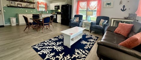 A living room with a sofa, armchairs, a coffee table, and a dining area with chairs and a table.