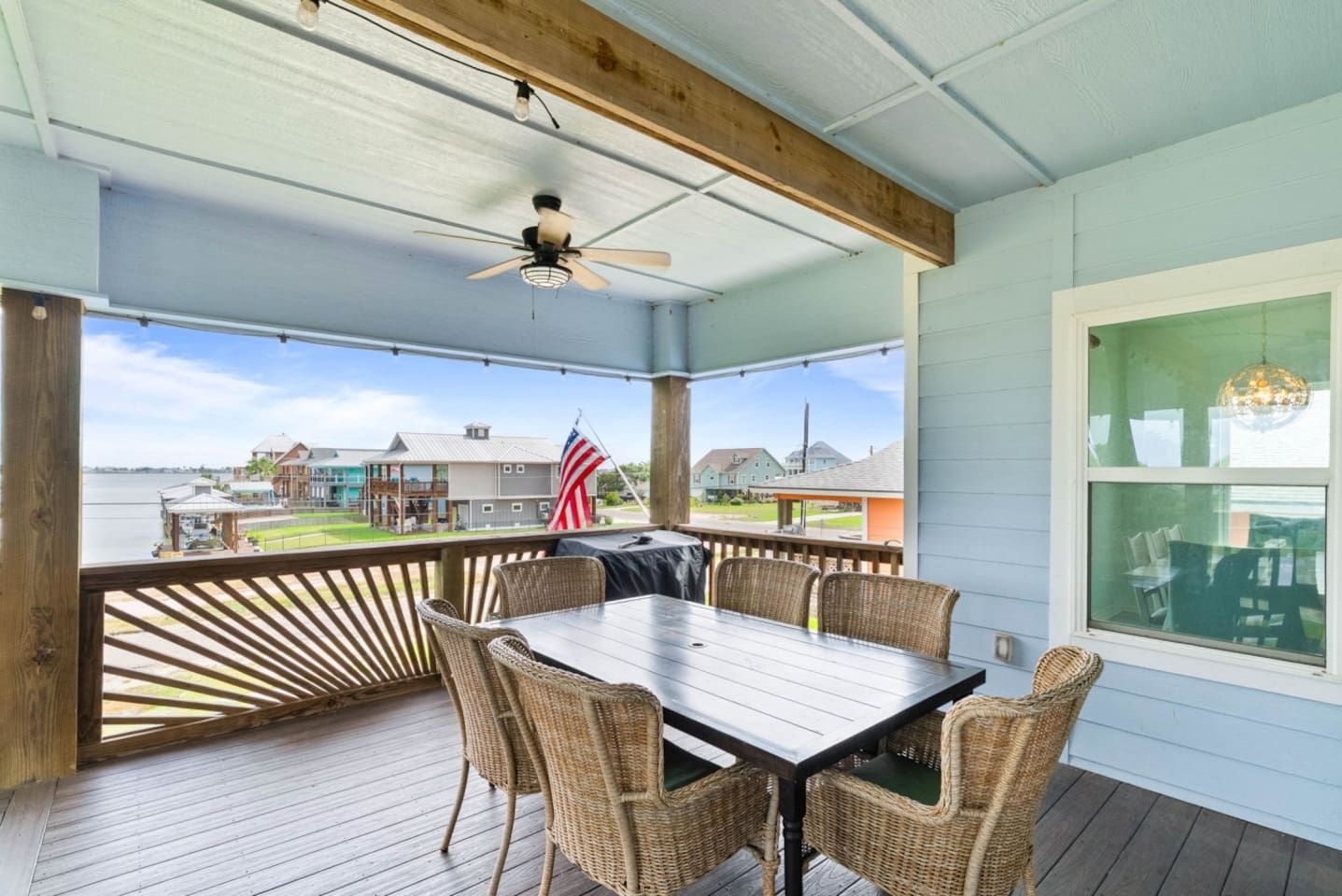 A covered outdoor area with a table and chairs, a ceiling fan, and an American flag.