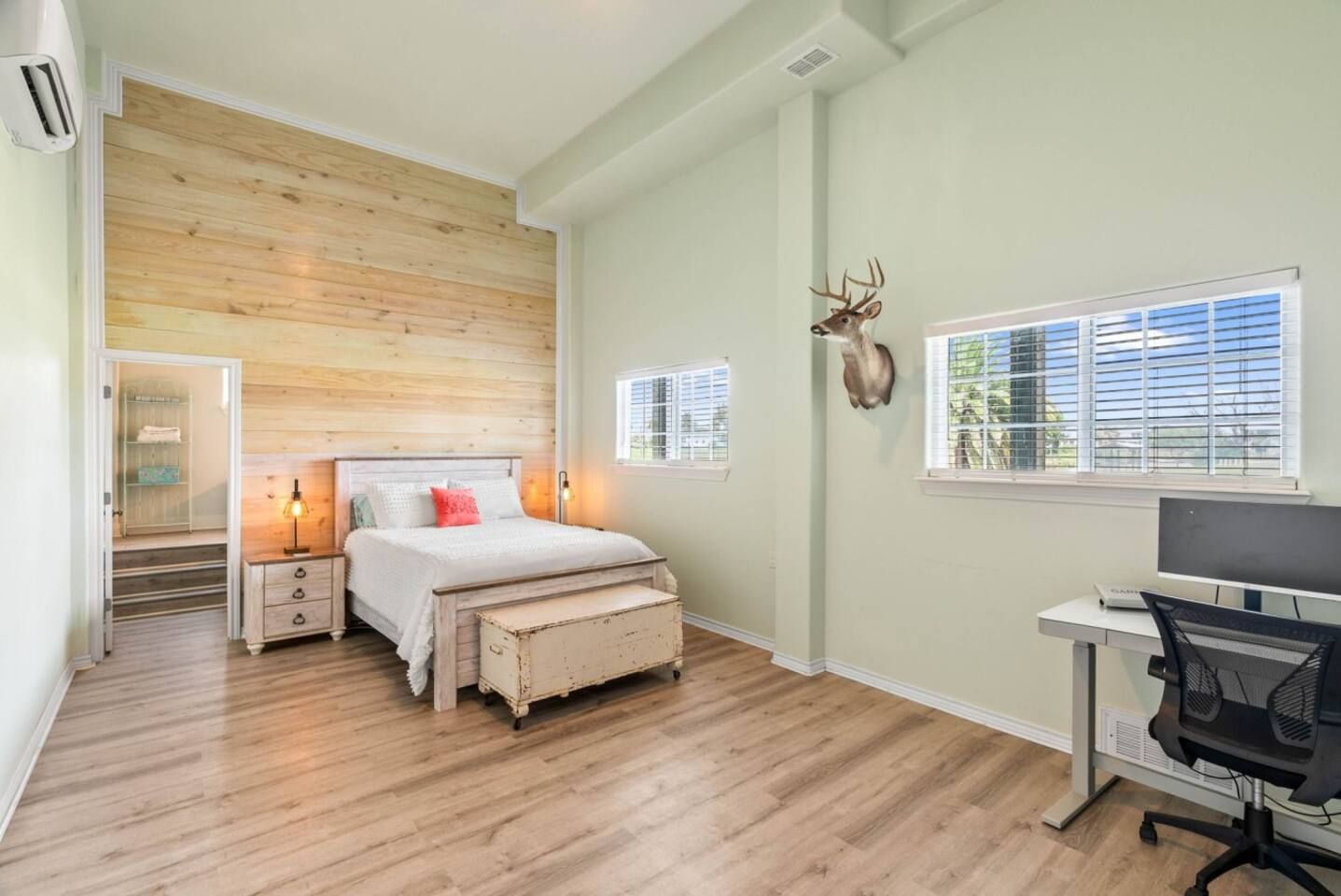 Une chambre avec un mur en bois, un lit, des tables de chevet, un bureau avec une chaise et une tête de cerf accrochée au mur.