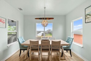 A dining room with a wooden table and chairs, a chandelier, and windows with a view. - Salty Vibes ~ Canal Front (Rockport)