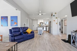 A modern living room with a blue leather sofa, a small table, and a kitchen in the background. - Copano Cove Retreat – Waterfront Relaxation (Rockport)