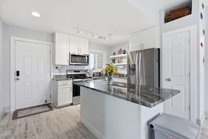 Una cocina moderna con armarios blancos, electrodomésticos de acero inoxidable y encimera de granito.