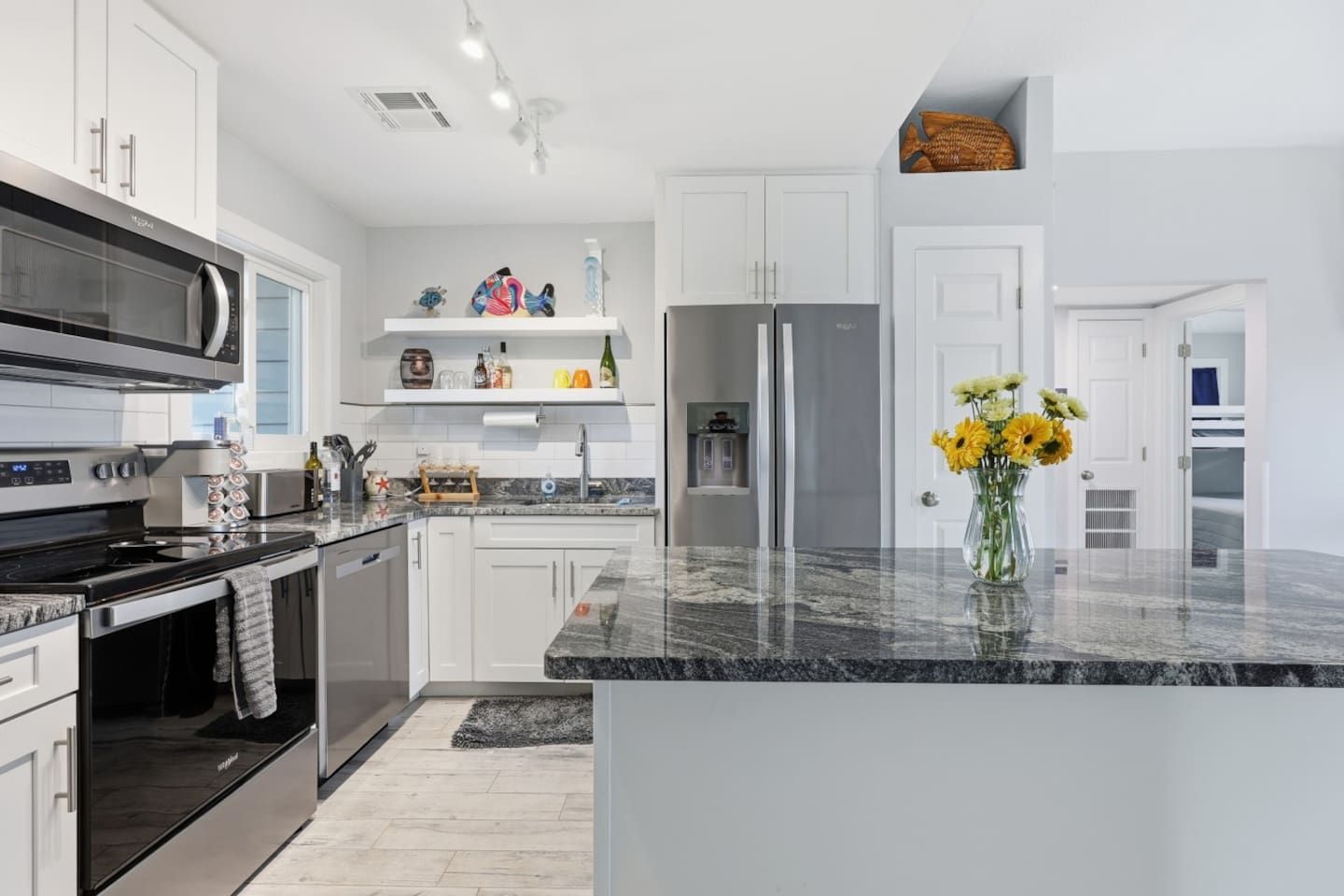 A modern kitchen with stainless steel appliances, white cabinetry, and a marble countertop.