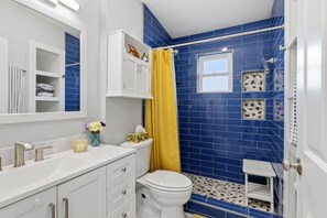 Ein Badezimmer mit weißem Waschtisch, Toilette und Duschbereich mit blauen Fliesen und einem gelben Duschvorhang.
