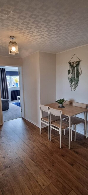 A dining area with a wooden table and chairs, a hanging macrame decoration, and a ceiling light fixture. - City View Apartment Edinburgh (Edinburgh)