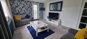 A living room with a sofa, a coffee table, a TV, and patterned wallpaper. - City View Apartment Edinburgh (Edinburgh)
