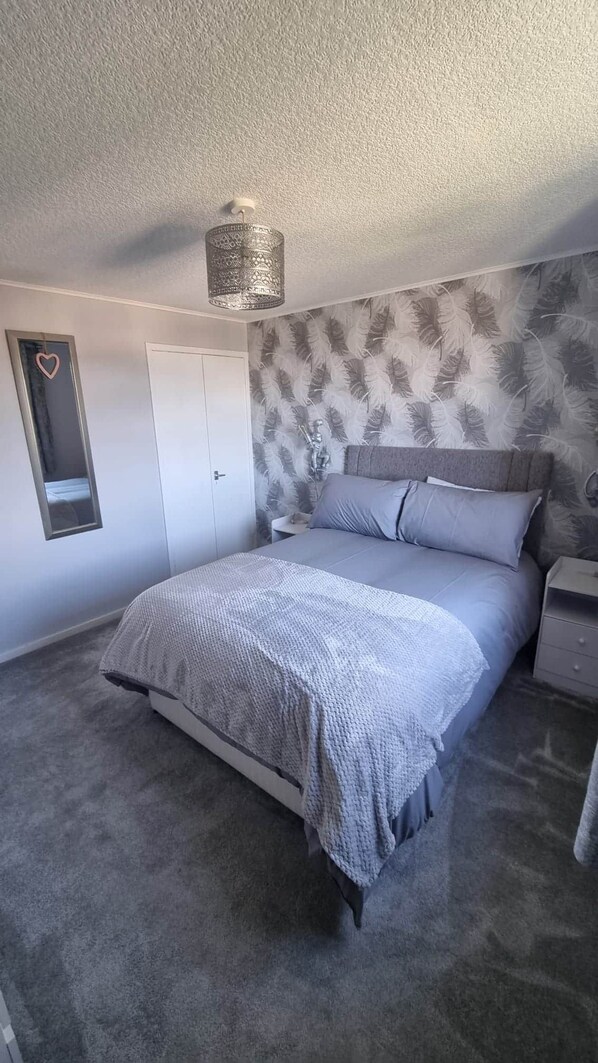 Un dormitorio con cama, mesita de noche, armario, espejo y lámpara en el techo.