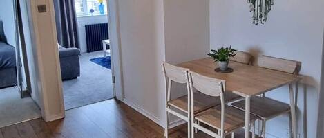 Et værelse med trægulv, et bord med stole, en hængende makramépynt og en loftlampe.