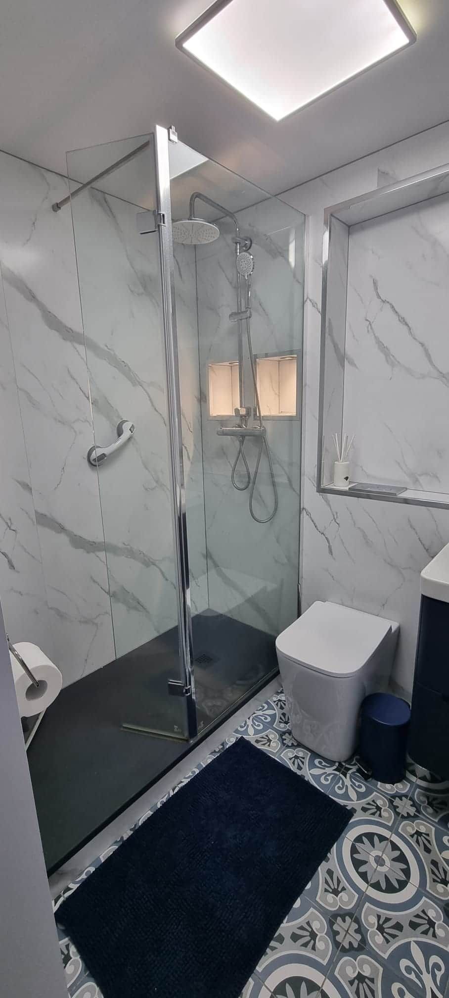 A modern bathroom with a glass-enclosed shower, a white sink, and a marble-patterned floor.