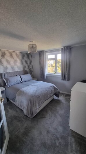 A bedroom with a bed, a nightstand, a dresser, a window with curtains, and a hanging light fixture. - City View Apartment Edinburgh (Edinburgh)