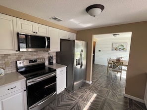 A modern kitchen with stainless steel appliances, white cabinetry, and a herringbone-patterned floor.