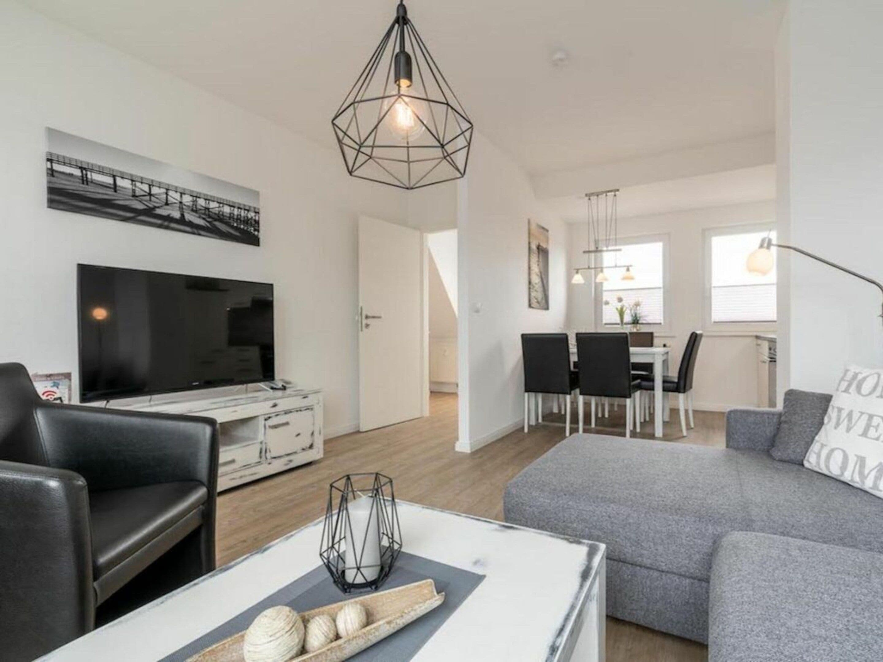 A modern living room with a grey sofa, a flat-screen TV, and a dining area with a table and chairs.