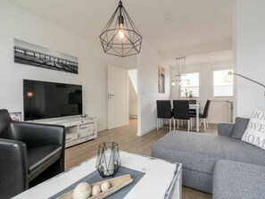 En moderne stue med en grå sofa, et fladskærms-tv og et spiseområde med et bord og stole.