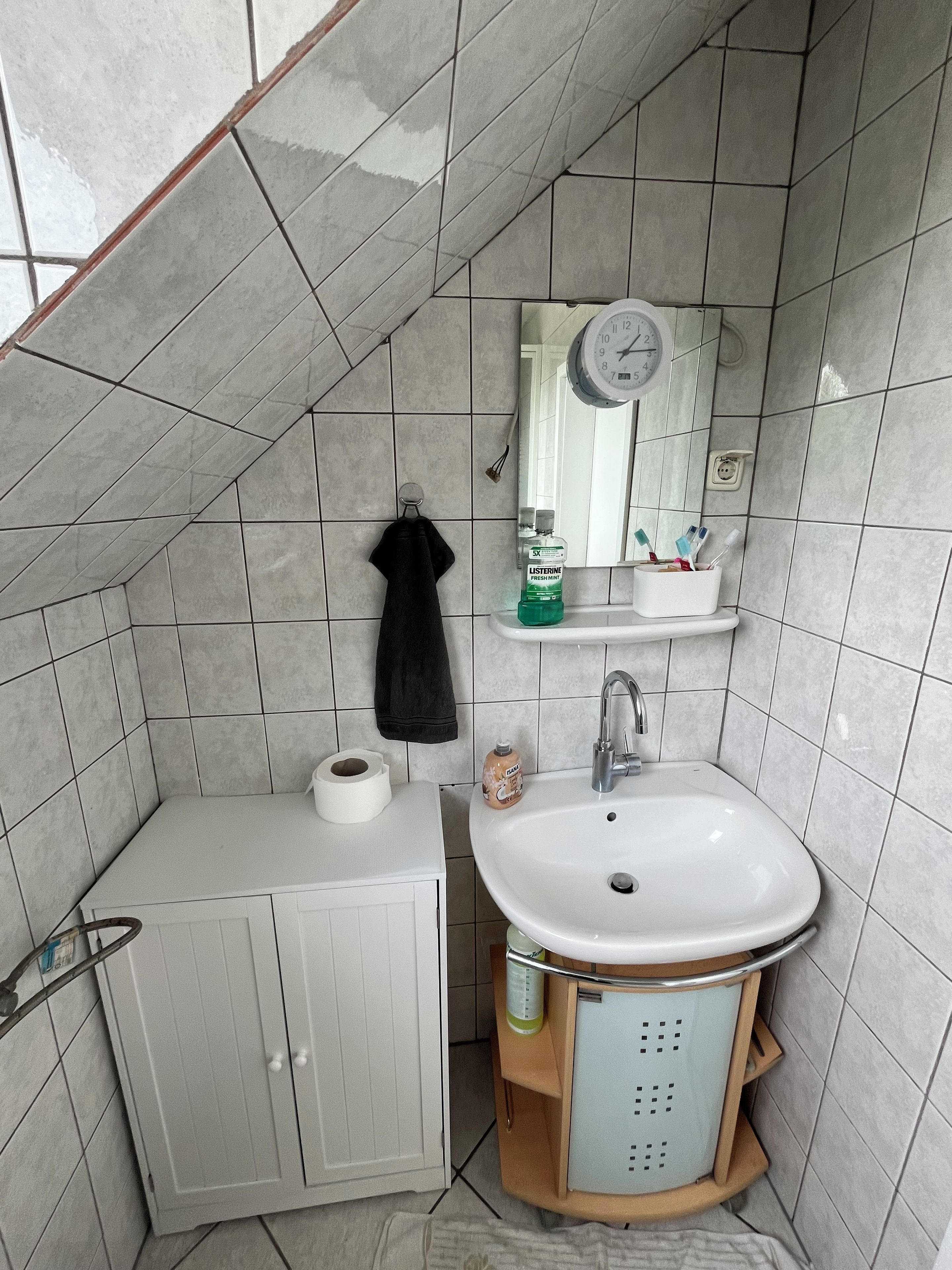 Une petite salle de bain avec des toilettes, un lavabo et un meuble. Une serviette est accrochée au mur, il y a une horloge et des articles de toilette sur le lavabo.
