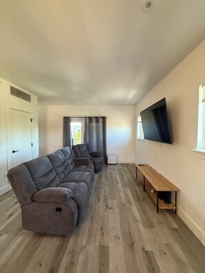 A modern living room with a sectional sofa, a flat-screen TV mounted on the wall, and a wooden bench. - New build 2-bedroom 2 Bath condo with AC in welcoming Bozeman (Bozeman)