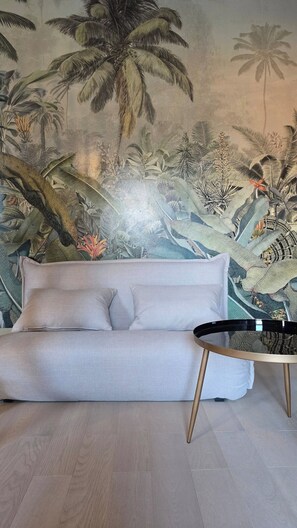 A room with a sofa and a coffee table, a tropical-themed wall mural, and a wooden floor.