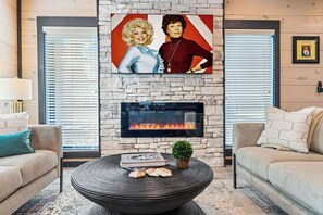Ein Wohnzimmer mit einem Kamin aus Stein, einem runden Couchtisch mit Büchern und einer Pflanze sowie zwei Sofas mit Kissen.