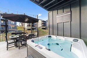 Een hottub op een terras buiten, met een tafel, stoelen, een barbecue en een bord met veiligheidsaanwijzingen.