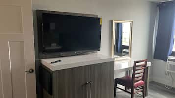 Una habitación con televisión sobre un mueble blanco, un espejo, una silla y una puerta.