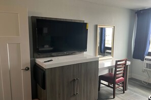 Quarto com televisão sobre um armário branco, um espelho, uma cadeira e uma porta.