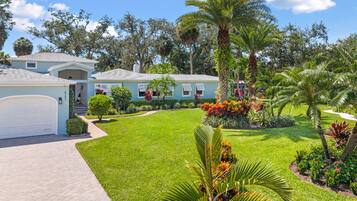 A residential property with a well-maintained lawn, a garage, and a variety of tropical plants.