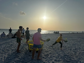 Eine Strandansicht mit Menschen, die verschiedene Aktivitäten ausüben, darunter ein Ballspiel mit Schlägern.