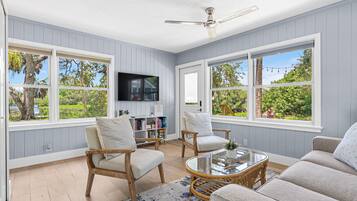 A spacious living room with large windows, a ceiling fan, and a flat-screen TV.