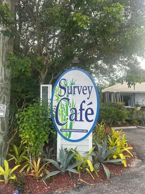 Une enseigne pour le café Survey, avec l’adresse de son site web, entourée de verdure et avec un bâtiment en arrière-plan.
