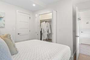 A bedroom with a bed, a closet with a robe hanging, and a door leading to another room.
