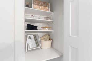 Interior blanco con un mueble empotrado que contiene toallas dobladas, una pequeña planta en maceta y un letrero de madera decorativo.