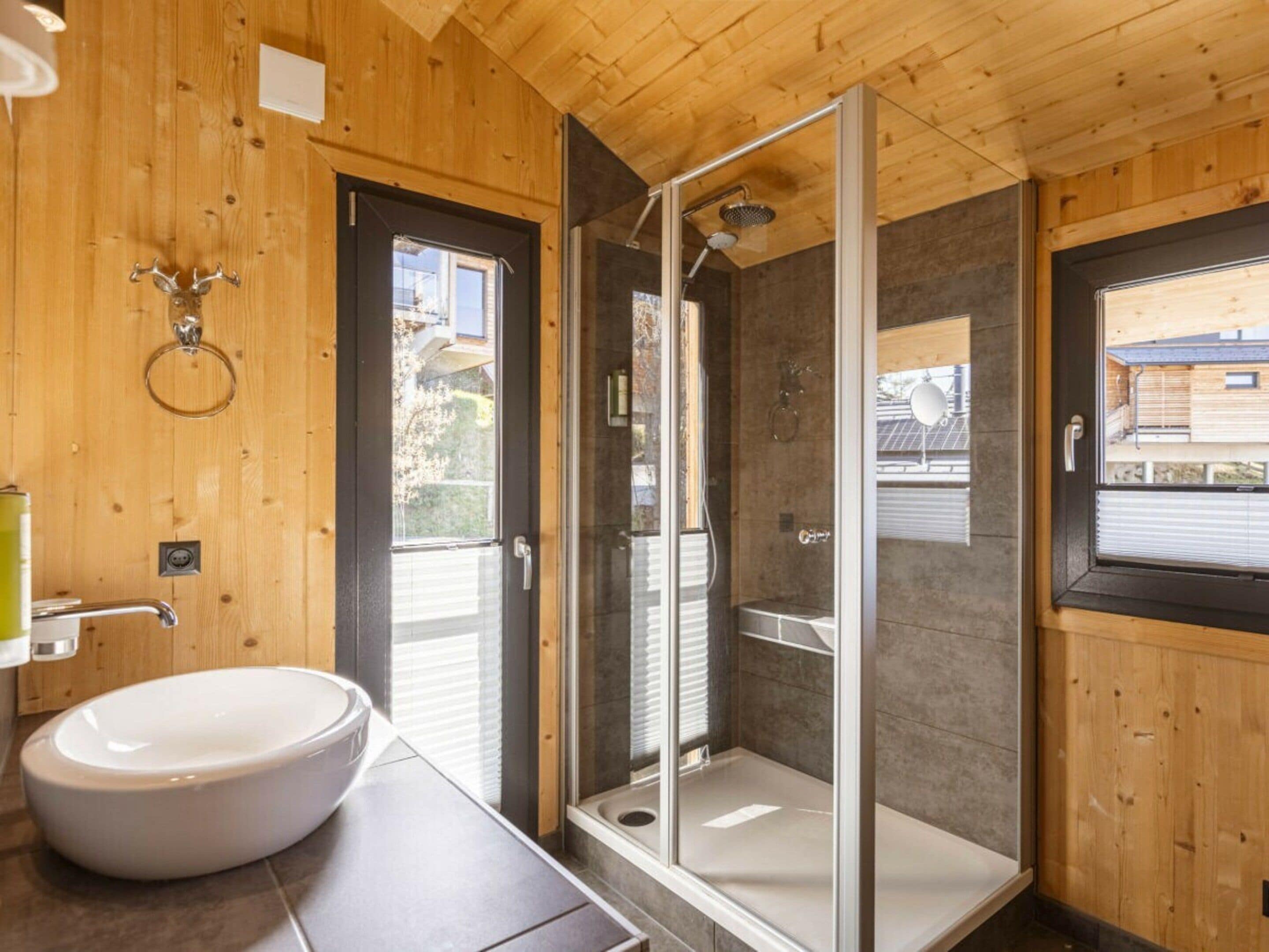 Ein Badezimmer mit einem großen weißen Waschbecken, einer Duschkabine aus Glas und Holzwänden.