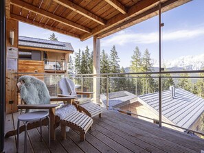 Eine Holzterrasse mit zwei Stühlen und einem Tisch, mit Blick auf eine gebirgige Landschaft.