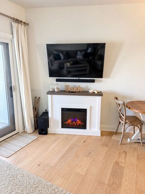 Ein Wohnzimmer mit Kamin, einem darüber montierten Fernseher und einem Essbereich mit Holztisch und Stühlen.