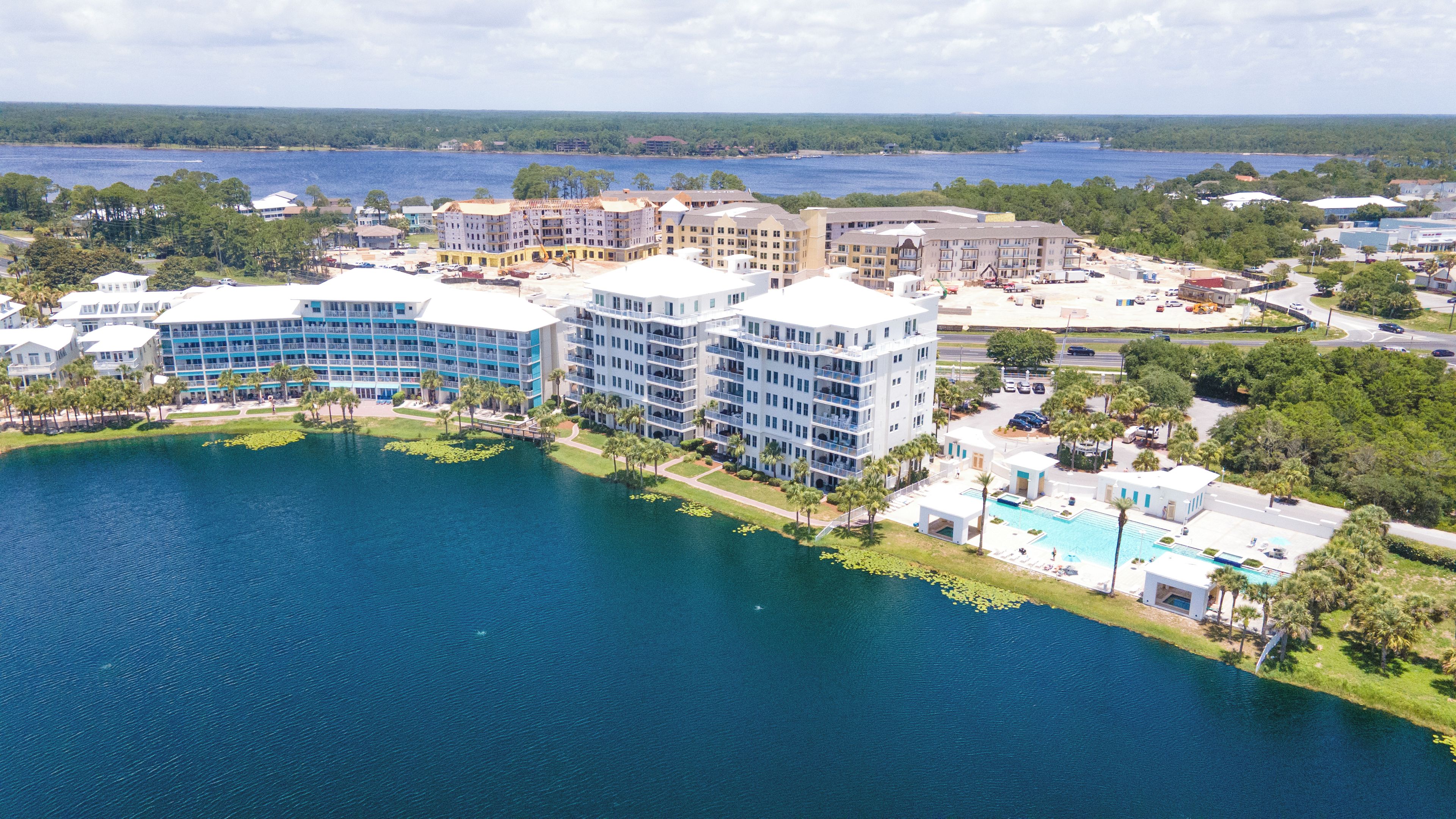 A multi-story hotel with a pool, surrounded by water and greenery. - The View at Carillon - Lake & Gulf Views + Resort Amenities (Panama City Beach)