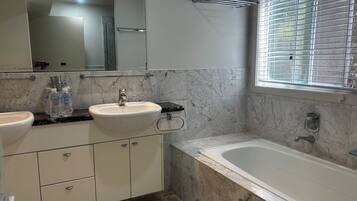 Ein Badezimmer mit einem Doppelwaschbecken, einem Spiegel, einer Badewanne und einem Fenster mit Jalousien.
