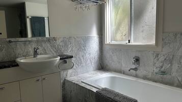 A bathroom with a marble sink, a bathtub, and a window.