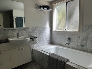 Ein Badezimmer mit Marmorwaschbecken, einer Badewanne und einem Fenster.