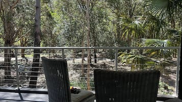 Un espacio de estar al aire libre cubierto con sillas de mimbre y un banco, con vistas a un paisaje natural con árboles y un camino.