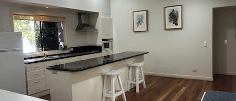 A modern kitchen with white cabinetry, a black countertop, a microwave, and two bar stools.