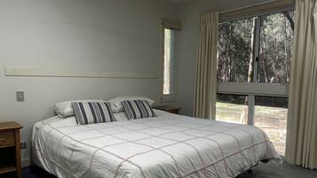 Un dormitorio con una cama grande, una mesita de noche, una ventana con cortinas y vistas a árboles.
