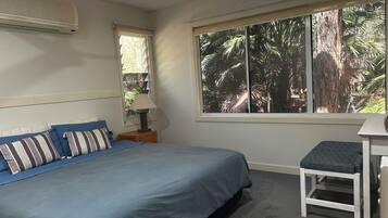 A bedroom with a bed, a nightstand, a lamp, a window with a view of trees, and a ceiling fan.