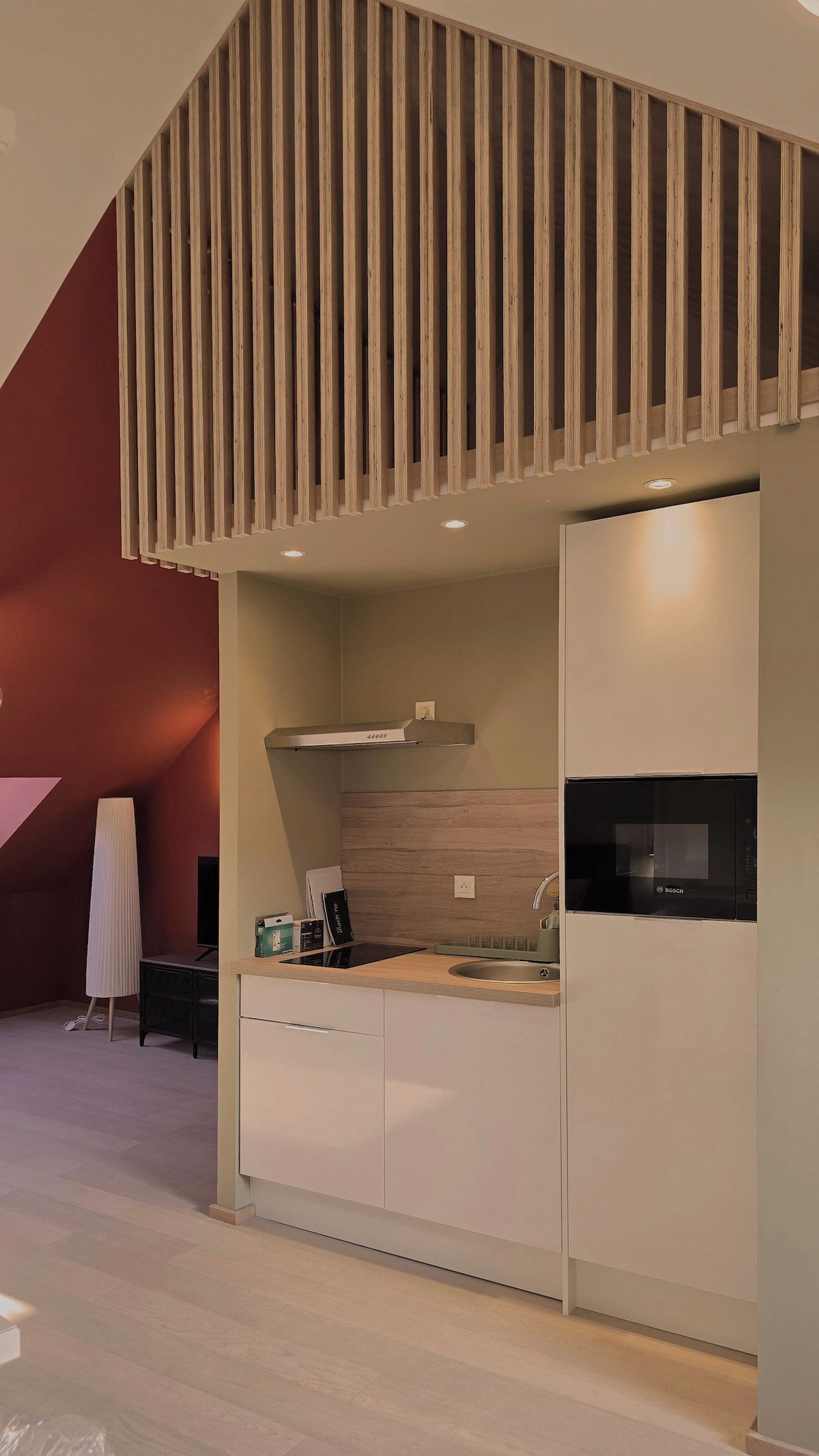 A modern kitchen with a built-in Bosch refrigerator, a stainless steel range hood, and a wooden slatted ceiling design.