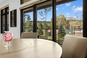 Habitació amb una taula rodona, un vas i vista a un paisatge de muntanyes a través de grans finestres.