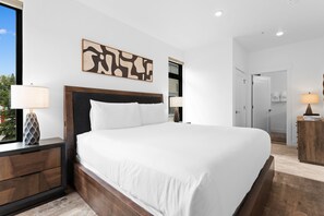 Ein modernes Hotelzimmer mit einem großen Bett, einem Nachttisch mit Lampe, einem Holz-Kopfschild und Blick ins Freie.