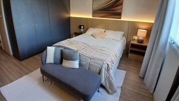 Una habitación de hotel con cama, mesitas de noche, un banco, un armario grande y un cuadro en la pared.