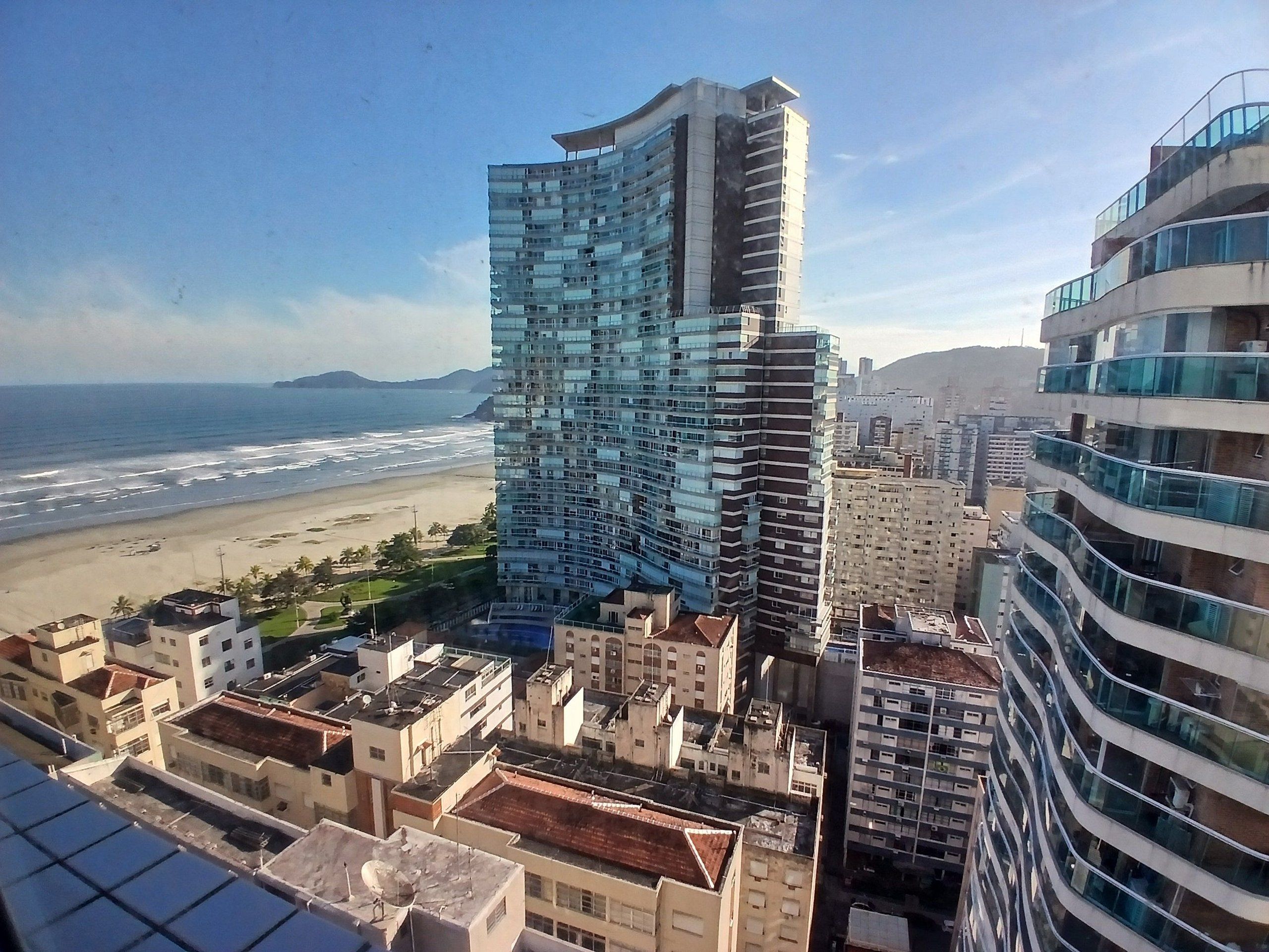 A high-rise building with a curved facade, adjacent to a beach and other residential buildings.