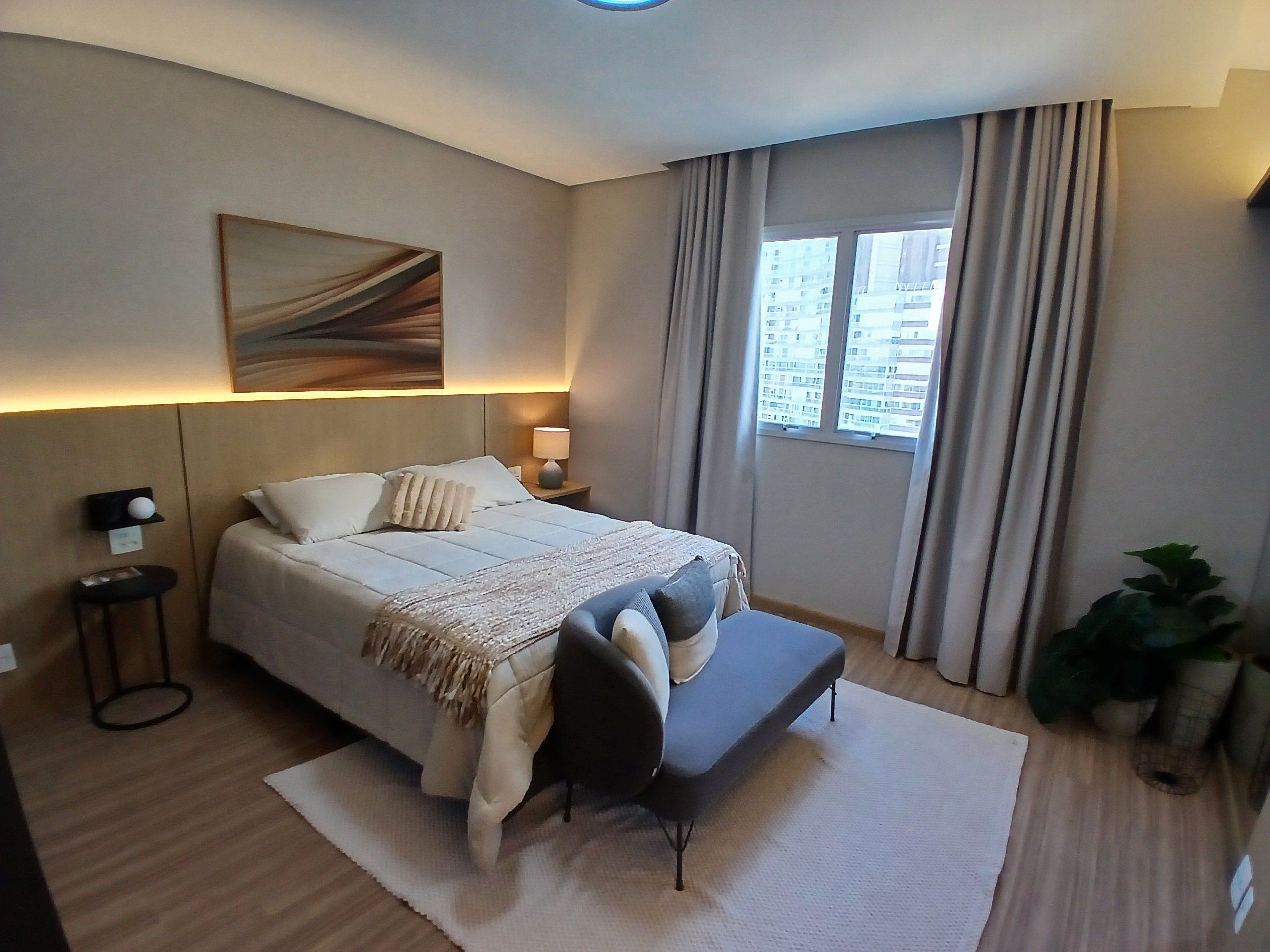 A modern hotel room with a large bed, bedside lamps, a bench, a large window with curtains, and a painting on the wall.